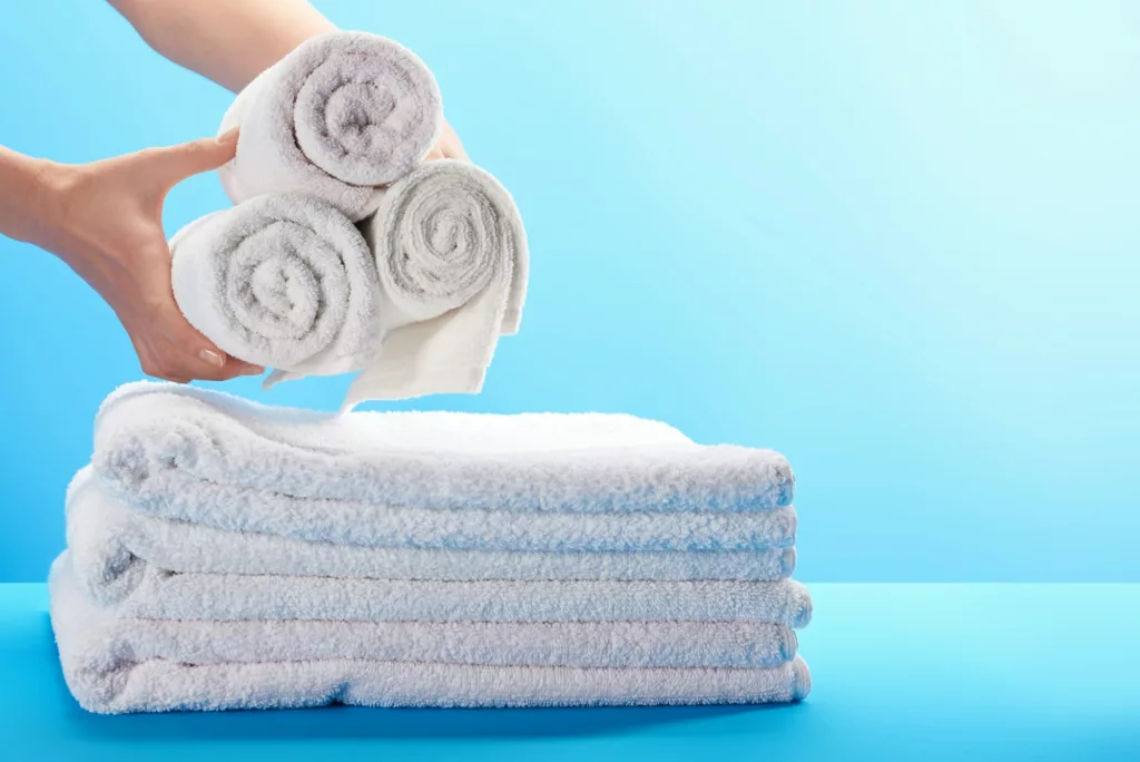 cropped shot of person holding rolled white towels above pile of towels on blue